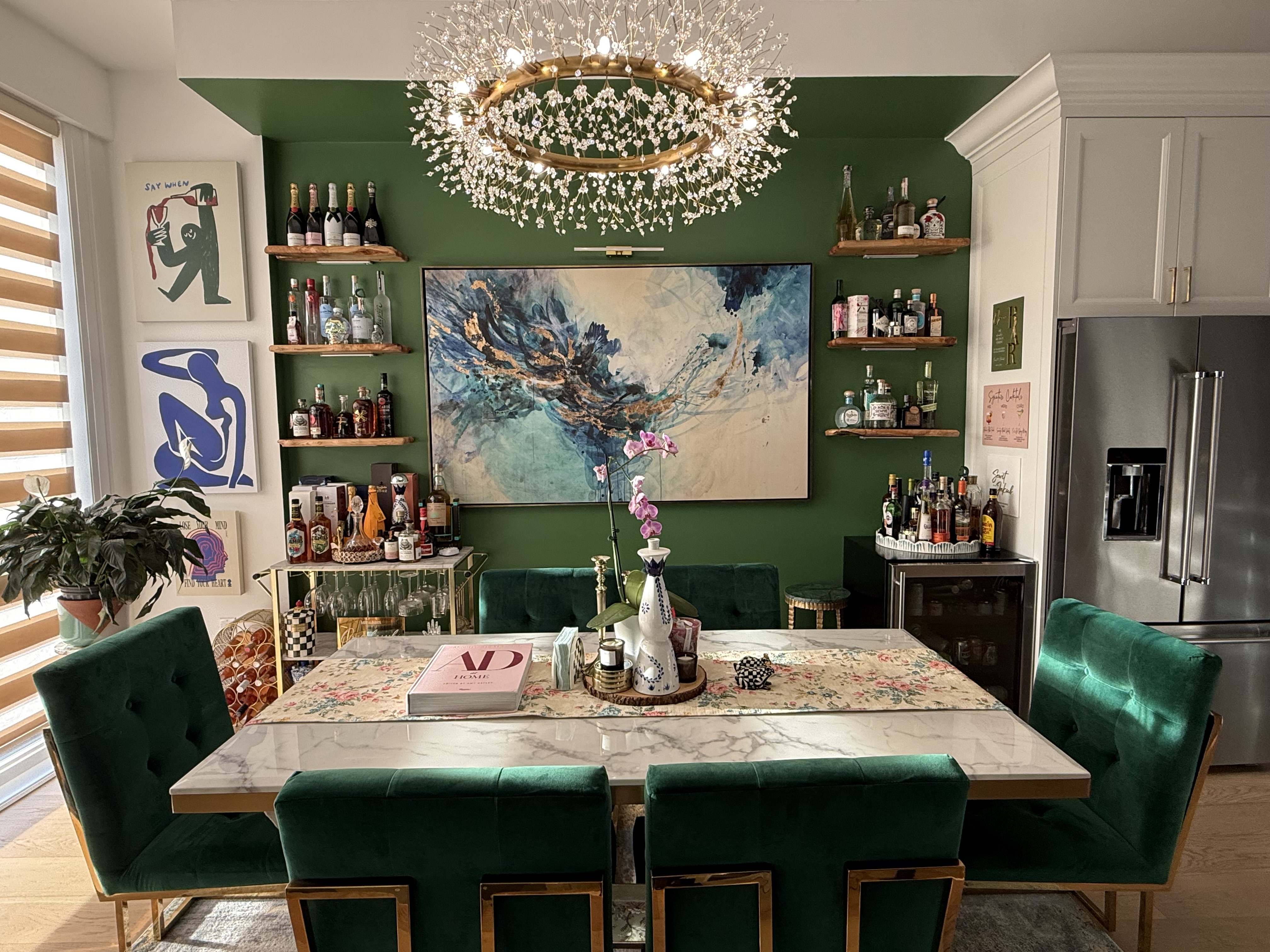 Sewit’s interior styling: emerald dining room with green feature wall, chandelier, central artwork, styled shelves and dining chairs